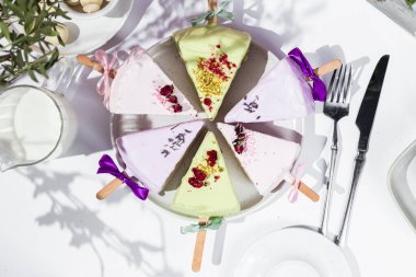 Masadaki beyaz tabakta çubuk üzerinde cheesecake. Cilalı cheesecake. Tatlı.