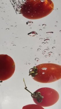 Suda hareketli kiraz domatesleri açık arkaplanda yakın plan