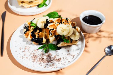 Masadaki beyaz tabakta muz ve çikolatalı Belçika waffle 'ları. Tatlı bir kahvaltı hazırlıyorum..