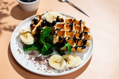 Masadaki beyaz tabakta muz ve çikolatalı Belçika waffle 'ları. Tatlı bir kahvaltı hazırlıyorum..