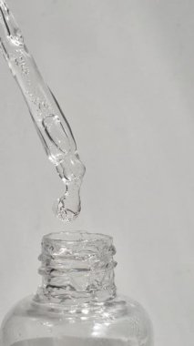 Beyaz arka planda cam bir pipetten damlayan şeffaf sıvı.