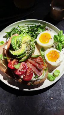 Somonlu sandviç, avokado, domates ve yumurta yakın plandaki beyaz tabakta. Sağlıklı kahvaltı.