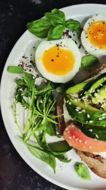 Somonlu sandviç, avokado, domates ve yumurta yakın plandaki beyaz tabakta. Sağlıklı kahvaltı.