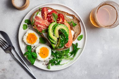  Somonlu sandviç, avokado, domates ve yumurta yakın plandaki beyaz tabakta. Sağlıklı kahvaltı.