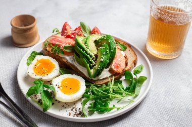  Somonlu sandviç, avokado, domates ve yumurta yakın plandaki beyaz tabakta. Sağlıklı kahvaltı.