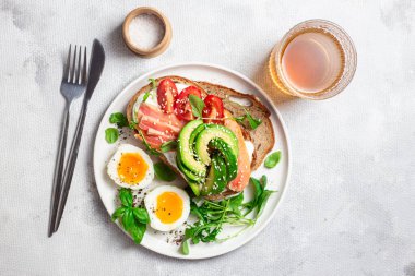  Somonlu sandviç, avokado, domates ve yumurta yakın plandaki beyaz tabakta. Sağlıklı kahvaltı.