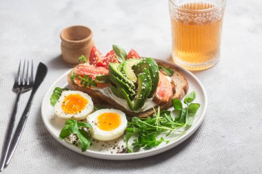  Somonlu sandviç, avokado, domates ve yumurta yakın plandaki beyaz tabakta. Sağlıklı kahvaltı.