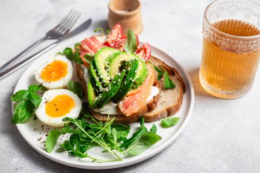  Somonlu sandviç, avokado, domates ve yumurta yakın plandaki beyaz tabakta. Sağlıklı kahvaltı.