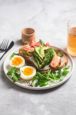  Somonlu sandviç, avokado, domates ve yumurta yakın plandaki beyaz tabakta. Sağlıklı kahvaltı.