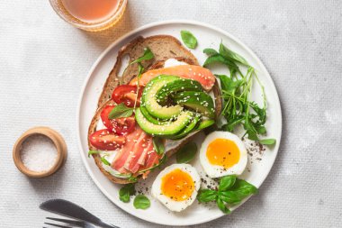  Somonlu sandviç, avokado, domates ve yumurta yakın plandaki beyaz tabakta. Sağlıklı kahvaltı.
