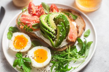  Somonlu sandviç, avokado, domates ve yumurta yakın plandaki beyaz tabakta. Sağlıklı kahvaltı.