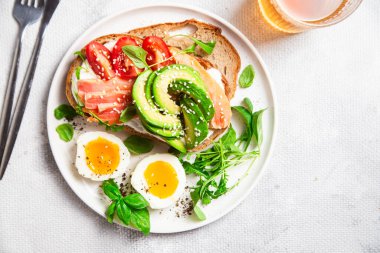 Somonlu sandviç, avokado, domates ve yumurta yakın plandaki beyaz tabakta. Sağlıklı kahvaltı.