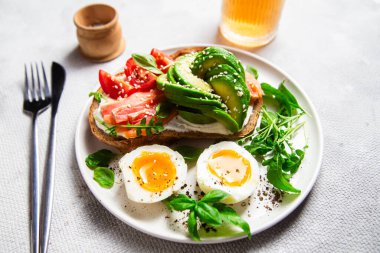  Somonlu sandviç, avokado, domates ve yumurta yakın plandaki beyaz tabakta. Sağlıklı kahvaltı.