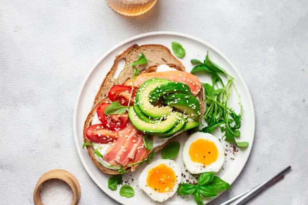  Somonlu sandviç, avokado, domates ve yumurta yakın plandaki beyaz tabakta. Sağlıklı kahvaltı.