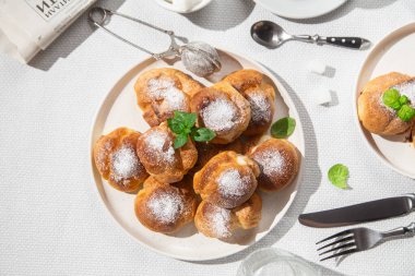 Masada beyaz bir tabakta kremalı profiterol. Kekler, kahve, tatlı..