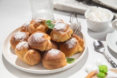 Masada beyaz bir tabakta kremalı profiterol. Kekler, kahve, tatlı..