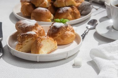 Masada beyaz bir tabakta kremalı profiterol. Kekler, kahve, tatlı..
