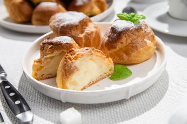 Masada beyaz bir tabakta kremalı profiterol. Kekler, kahve, tatlı..