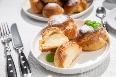 Masada beyaz bir tabakta kremalı profiterol. Kekler, kahve, tatlı..