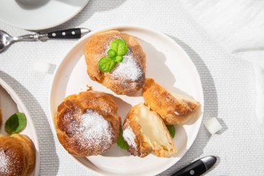 Masada beyaz bir tabakta kremalı profiterol. Kekler, kahve, tatlı..