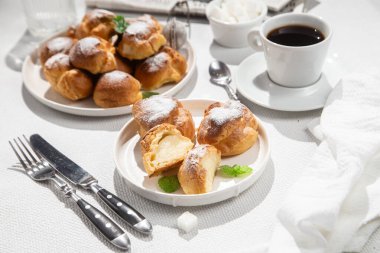 Masada beyaz bir tabakta kremalı profiterol. Kekler, kahve, tatlı..