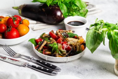 Domatesli taze patlıcan salatası ve beyaz tabakta fesleğen.