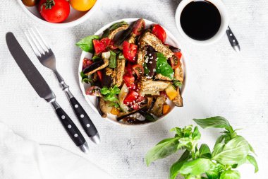 Domatesli taze patlıcan salatası ve beyaz tabakta fesleğen.