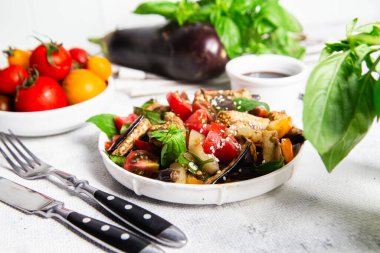 Domatesli taze patlıcan salatası ve beyaz tabakta fesleğen.