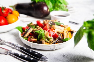 Domatesli taze patlıcan salatası ve beyaz tabakta fesleğen.