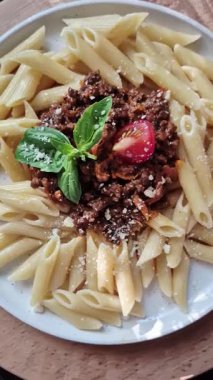 Beyaz tabakta bolonez soslu makarna ve fesleğen.