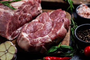 Ahşap bir tahtada çiğ domuz eti, otlar ve domateslerle pişirilmeye hazır.