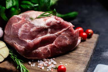 Ahşap bir tahtada çiğ domuz eti, otlar ve domateslerle pişirilmeye hazır.