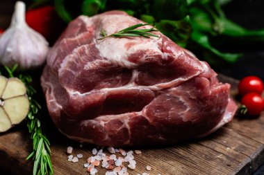 Ahşap bir tahtada çiğ domuz eti, otlar ve domateslerle pişirilmeye hazır.