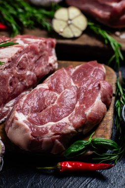 Ahşap bir tahtada çiğ domuz eti, otlar ve domateslerle pişirilmeye hazır.