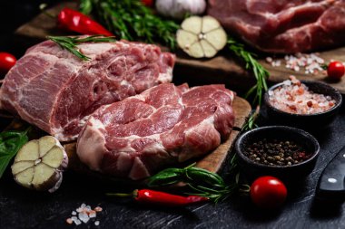 Ahşap bir tahtada çiğ domuz eti, otlar ve domateslerle pişirilmeye hazır.