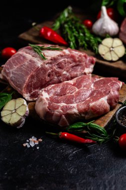 Ahşap bir tahtada çiğ domuz eti, otlar ve domateslerle pişirilmeye hazır.