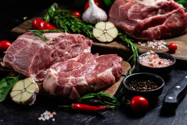 Ahşap bir tahtada çiğ domuz eti, otlar ve domateslerle pişirilmeye hazır.