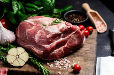 Ahşap bir tahtada çiğ domuz eti, otlar ve domateslerle pişirilmeye hazır.