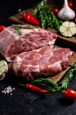 Ahşap bir tahtada çiğ domuz eti, otlar ve domateslerle pişirilmeye hazır.