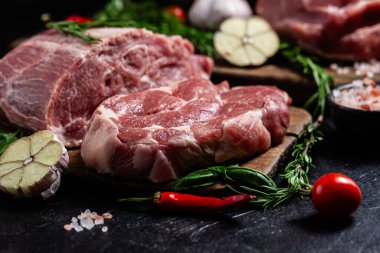 Ahşap bir tahtada çiğ domuz eti, otlar ve domateslerle pişirilmeye hazır.