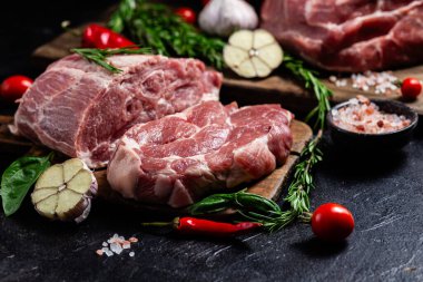 Ahşap bir tahtada çiğ domuz eti, otlar ve domateslerle pişirilmeye hazır.