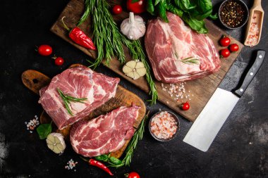 Ahşap bir tahtada çiğ domuz eti, otlar ve domateslerle pişirilmeye hazır.