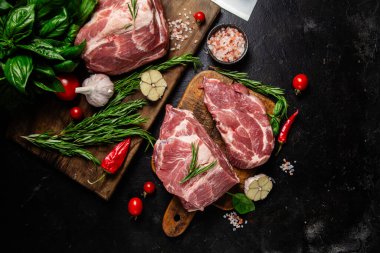 Ahşap bir tahtada çiğ domuz eti, otlar ve domateslerle pişirilmeye hazır.