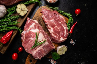 Ahşap bir tahtada çiğ domuz eti, otlar ve domateslerle pişirilmeye hazır.