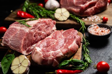 Ahşap bir tahtada çiğ domuz eti, otlar ve domateslerle pişirilmeye hazır.