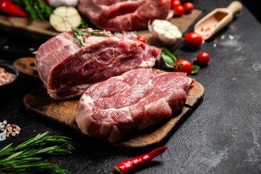 Ahşap bir tahtada çiğ domuz eti, otlar ve domateslerle pişirilmeye hazır.