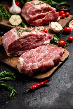 Ahşap bir tahtada çiğ domuz eti, otlar ve domateslerle pişirilmeye hazır.