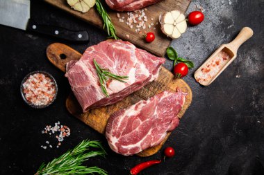 Ahşap bir tahtada çiğ domuz eti, otlar ve domateslerle pişirilmeye hazır.