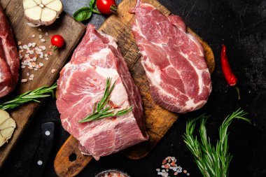 Ahşap bir tahtada çiğ domuz eti, otlar ve domateslerle pişirilmeye hazır.