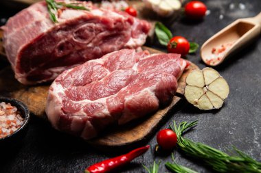 Ahşap bir tahtada çiğ domuz eti, otlar ve domateslerle pişirilmeye hazır.